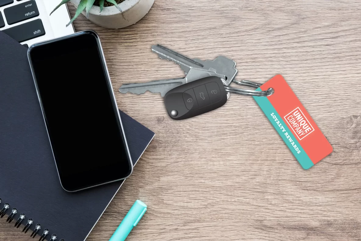 key tag with car key fob on wooden desk next to phone and notebook