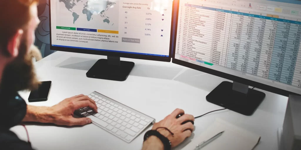 Man working on spreadsheets dual screens.